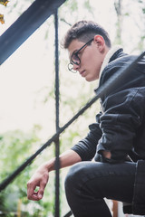 a young rebel in a jacket and jeans on the background of an old crumbling building with glasses and...