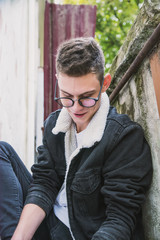a young rebel in a jacket and jeans on the background of an old crumbling building with glasses and...