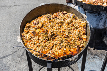 Obraz na płótnie Canvas Traditional dish of oriental cuisine - pilaf with meat in a larger vat on the street during the festival