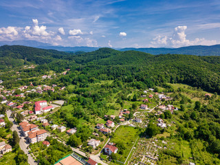 Drone view over the green forest and small city in mountainous area sunny day in summer season. Carpatians mountains, Romania.