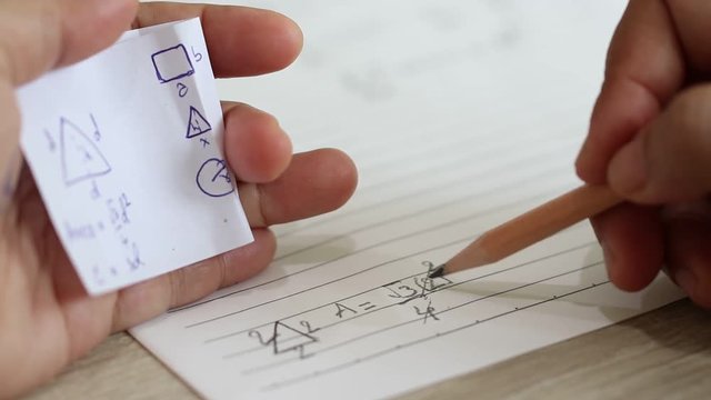 Student using formula math sheet to cheat on test. Hand of university student holding pencil doing math question in examination and cheating in test with answer piece of paper in hand. 