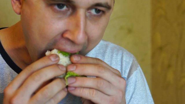Cute young hungry caucasian man with an appetite is eating a tasty and juicy sandwich, carefully chewing up a close-up, slow motion