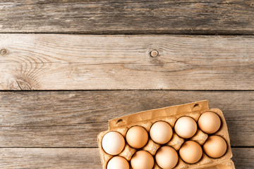 Fresh eggs in carton box on wooden background. Top view