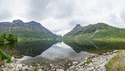 Fototapeta na wymiar Panorama of beautiful Overdalen valley. Reflections of the slopes in the mountain lake, symmetrical centered scene. Cloudy summer day in Norway, Scandinavian pearl.