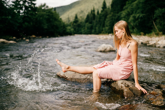 Young happy girl kicking foot in river and splashing water.