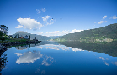 Panoramic view of The Sognefjord (Sognefjorden), nicknamed the King of the Fjords. Te largest and deepest fjord in Norway. Symmetry created by reflections in the still ocean water. Bright midsummer.