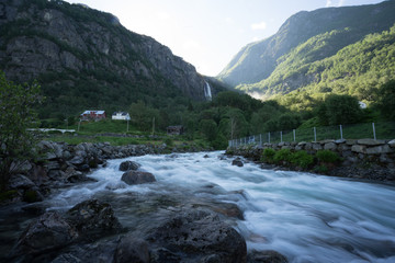 Idyllic setting on the southern side of the Lusterfjord. Magnificent view  early midsummer morning. Streaming river. 218 metre high Feigefossen (Feigumfossen) waterfall in the background. Norway.