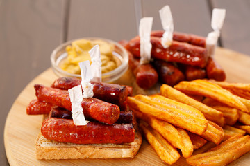 Spicy sausages on toast bread with fried potato on wooden plate , wood background.