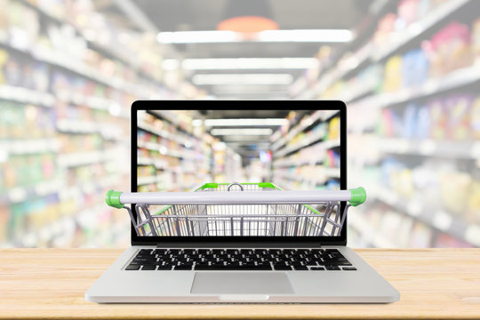 supermarket aisle blurred background with laptop computer and shopping cart on wood table grocery online concept