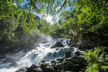 Magnificent view  early midsummer morning in Norway. Hike through the forest to 218 metre high Feigefossen (Feigumfossen) waterfall. Mystical feeling, sun shining through the foliage, river streaming.