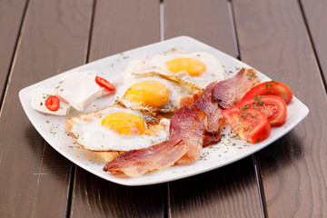 Healthy bacon fried egg on toast bread breakfast on plate , fresh tomatoes and cheese on plate , wood background.