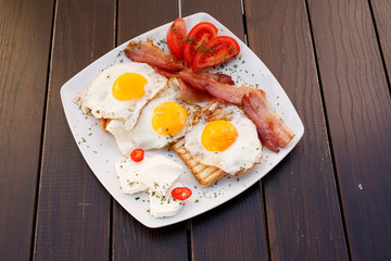 Healthy bacon fried egg on toast bread breakfast on plate , fresh tomatoes and cheese on plate , wood background.