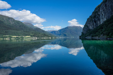 Fototapeta na wymiar Panoramic view of The Sognefjord (Sognefjorden), nicknamed the King of the Fjords. Te largest and deepest fjord in Norway. Symmetry created by reflections in the still ocean water. Bright midsummer.