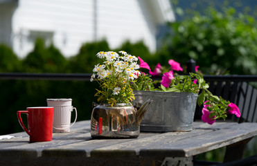 Table with shiny teapot and vintage bowl both used as flower pots. Colorful blossoms, wooden rustic plate. Cafe in Solvorn, a cute small resort village.  Midsummer day in Norway.