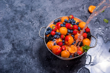 Water splashing on fresh summer fruits and berries, apricots, blueberries, strawberries in colander, washing fruits and berries, vegan healthy food