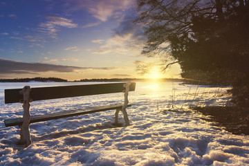 Fototapeta na wymiar Bench at a shore during winter with sun shining in the background