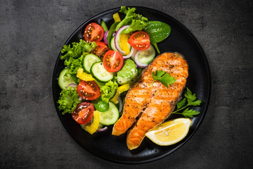 Grilled salmon fish steak with vegetables on black.