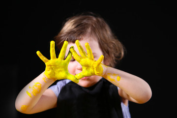 Baby pens, smeared in yellow paint. The face is out of focus. The concept of children's creativity and work in kindergarten or school. Enhancements and hobbies in childhood.