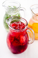 Cold and refreshing citrus cocktail with grapefruit and orange, strawberry, apple, lemon and herbs. Water for detox or dieting in glass jug on white background, copy space. Homemade drink.