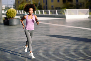 Black woman, afro hairstyle, running outdoors in urban road.