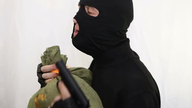 Young saucy caucasian robber with a gun dances with a bag of money and rejoices at the prey, close-up