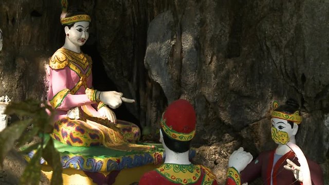 Steady, medium close up shot of multiple statues depicting a scene of Buddha teaching children.