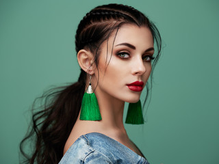 Brünettes Mädchen mit perfektem Make-up. Schöne vorbildliche Frau mit lockiger Frisur. Pflege- und Schönheitsprodukte für das Haar. Dame mit geflochtenem Haar. Modell mit Schmuck. Türkisfarbener Hintergrund © Oleg Gekman