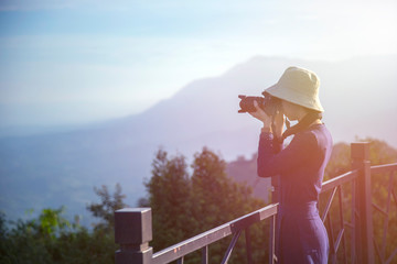 Fototapeta na wymiar Woman holding camera for take a photo with mountain view and ray of sunrise. Vacation travel in holiday concept.