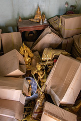 The storage room with mess of a pile of peper boxes and sacred objects incl.Buddha statues in the Buddhist temple, Thailand.
