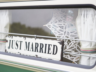 A just married sign hangs in the back window of a vehicle.White umbrella can be seen in background - Image