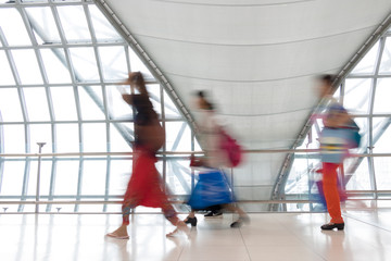 A people with luggage walking in motion blur on white corridor with large windows. Blurred people walking in a modern building. Abstract image of people in the lobby.