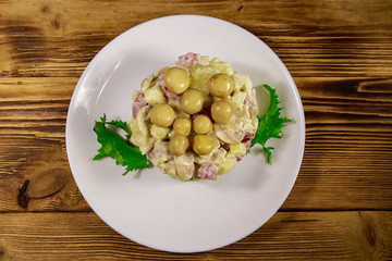 Potato salad with marinated mushrooms, sausage, onion and mayonnaise on wooden table
