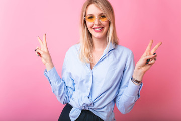 Portrait of gorgeous blond woman 30s in stylish outfit smiling and looking at camera isolated over pink background. V sign gesture, copy space