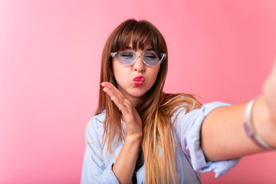Studio portrait of beautiful woman smiling with white teeth and making selfie, photographing herself over pink background. Girl Taking Selfie Picture With Duck Face Lips Smart Phone Photo 