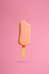 pink ice cream popsicle on pink background bitten off a piece hanging in the air