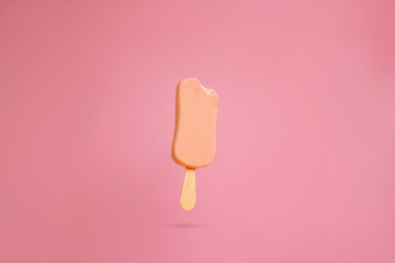 pink ice cream popsicle on pink background bitten off a piece hanging in the air
