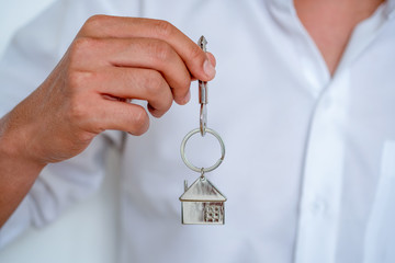 Real estate agent handing over house keys, Men hand holding key with house shaped keychain, Close up focus.