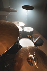 Modern drum set prepared for playing in a dark rehearsal room on stage with a bright spotlight. The...
