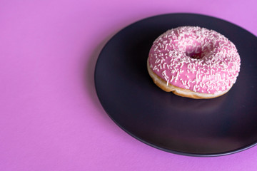 Close-up. Fresh tasty strawberry pink donut, in icing and sprinkling on a plate on the right on a pink background.  