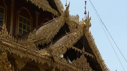 A daylight closeup shot of a Buddhist temple s exterior showing the intricate decorative ornamentation of the building s roof and window moldings in matching gold paint.