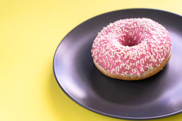 Fresh tasty strawberry donut, in icing and sprinkling on a plate on a yellow background. 