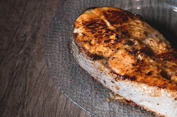 Close-up one grilled cum salmon keta fish steak on a glass transparent plate on a dark wood table background. A little overdone dish. Sea food for lovers of fried