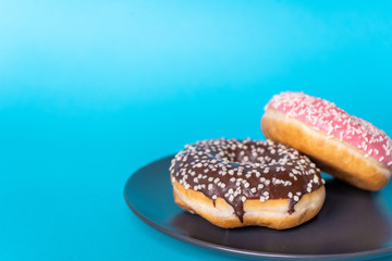 Close-up of fresh tasty donuts: chocolate and strawberry, in icing and sprinkling on a plate on a blue background