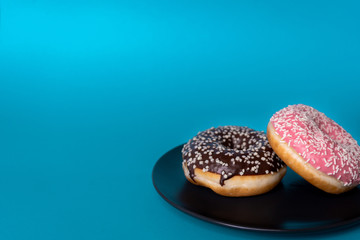Fresh tasty donuts: chocolate and strawberry, in icing and sprinkling on a plate on a blue background