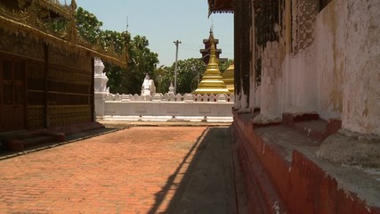 A steady medium shot of a Buddhist museum s building exterior showing the brick walkway leading to the golden pagoda that is enclosed in a cement fence and painted in white, taken in a very sunny day.