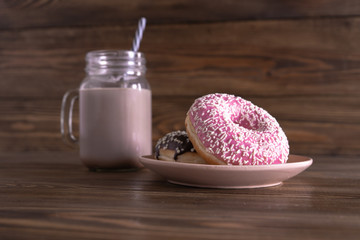 A glass mug of coffee with the tube and fresh tasty chocolate and strawberry donuts on a plate on the wooden background. Side view. 