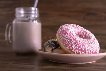 A glass mug of coffee with the tube and fresh tasty chocolate and strawberry donuts on a plate on the wooden background. Side view. Close-up