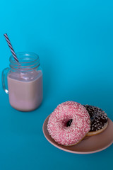 A glass mug of coffee with the tube and fresh tasty chocolate and strawberry donuts on a plate on a blue background. Vertical. Close-up