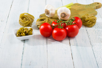 fresh tomato, garlic, olive, uncooked tagliatelle pasta on white wooden