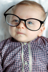 Baby boy with glasses. Adorable face, children funny pose. Lying on bed with glasses, genius kid. 